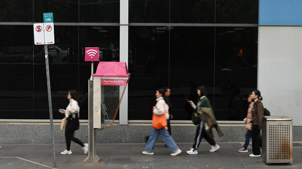 People walk past a Telstra payphone