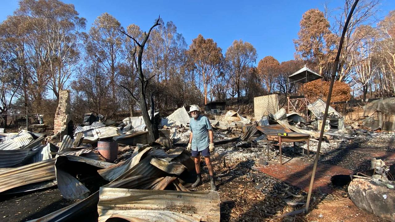 A man stands surrounded by fire-damaged roofing iron and debris.