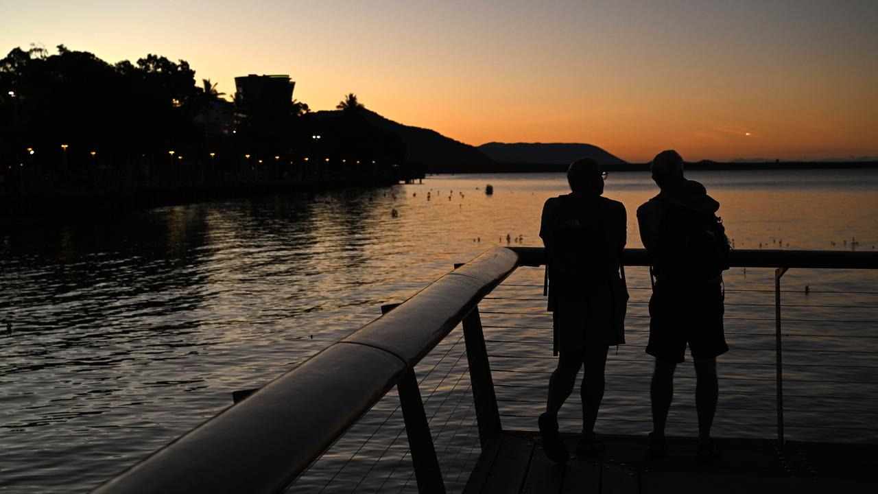 People are seen on the Cairns Esplanade as the sun sets